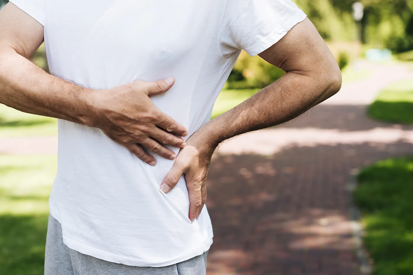 Man experiencing lower back pain outdoors – seasonal strain injuries from yard work.
