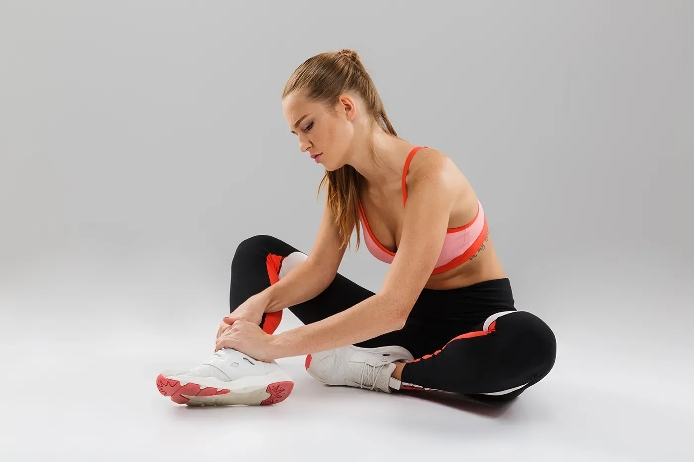 Woman sitting on floor reaching toward her foot — back to sports season flexibility exercise.