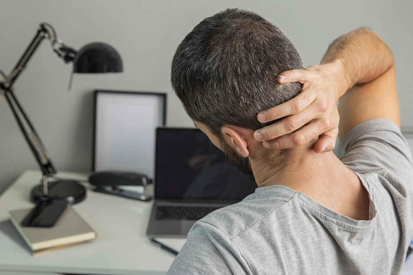man with neck pain from poor posture while working remotely