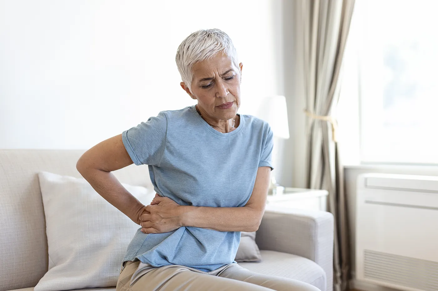 Senior woman experiencing lower back pain on sofa, chiropractic for sciatica help at Blair Chiropractic & Massage Therapy